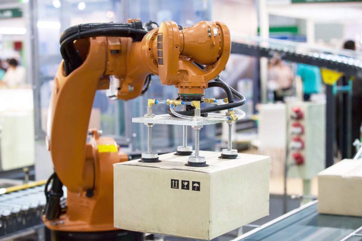 Línea de producción automatizada con brazo robótico levantando una caja.