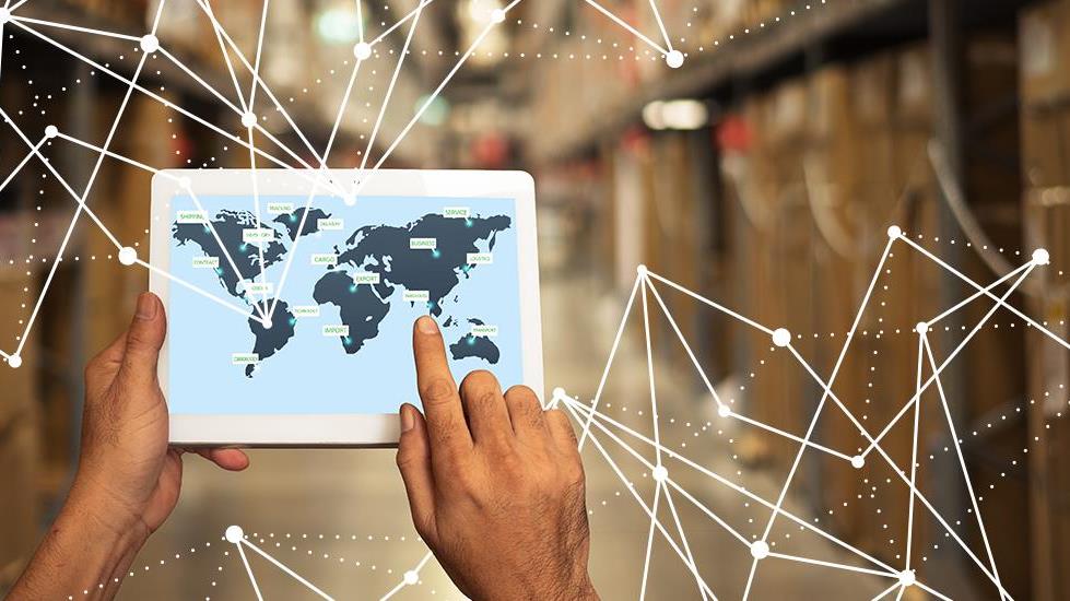 Una persona usa una tableta para acceder a un mapa mundial en 2D mientras está de pie en una fábrica