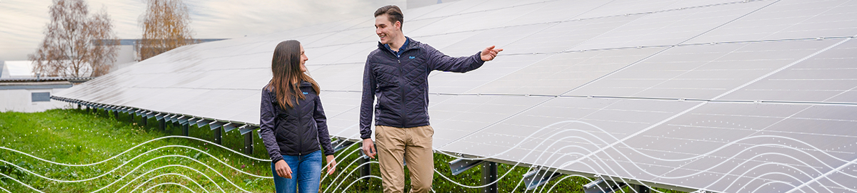 Zwei Flex-Mitarbeiter laufen vor Solarmodulen auf einer grünen Wiese